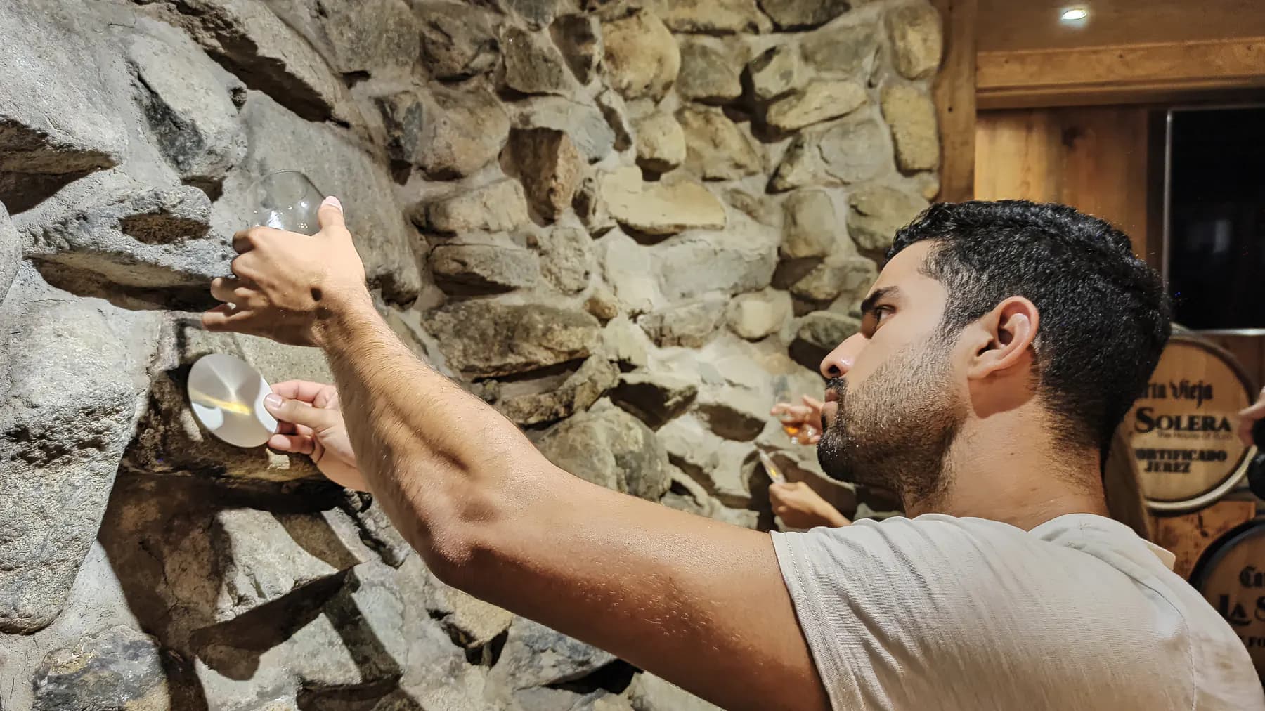 A guest raising a glass of rum to the light during a tasting in a stone-walled room