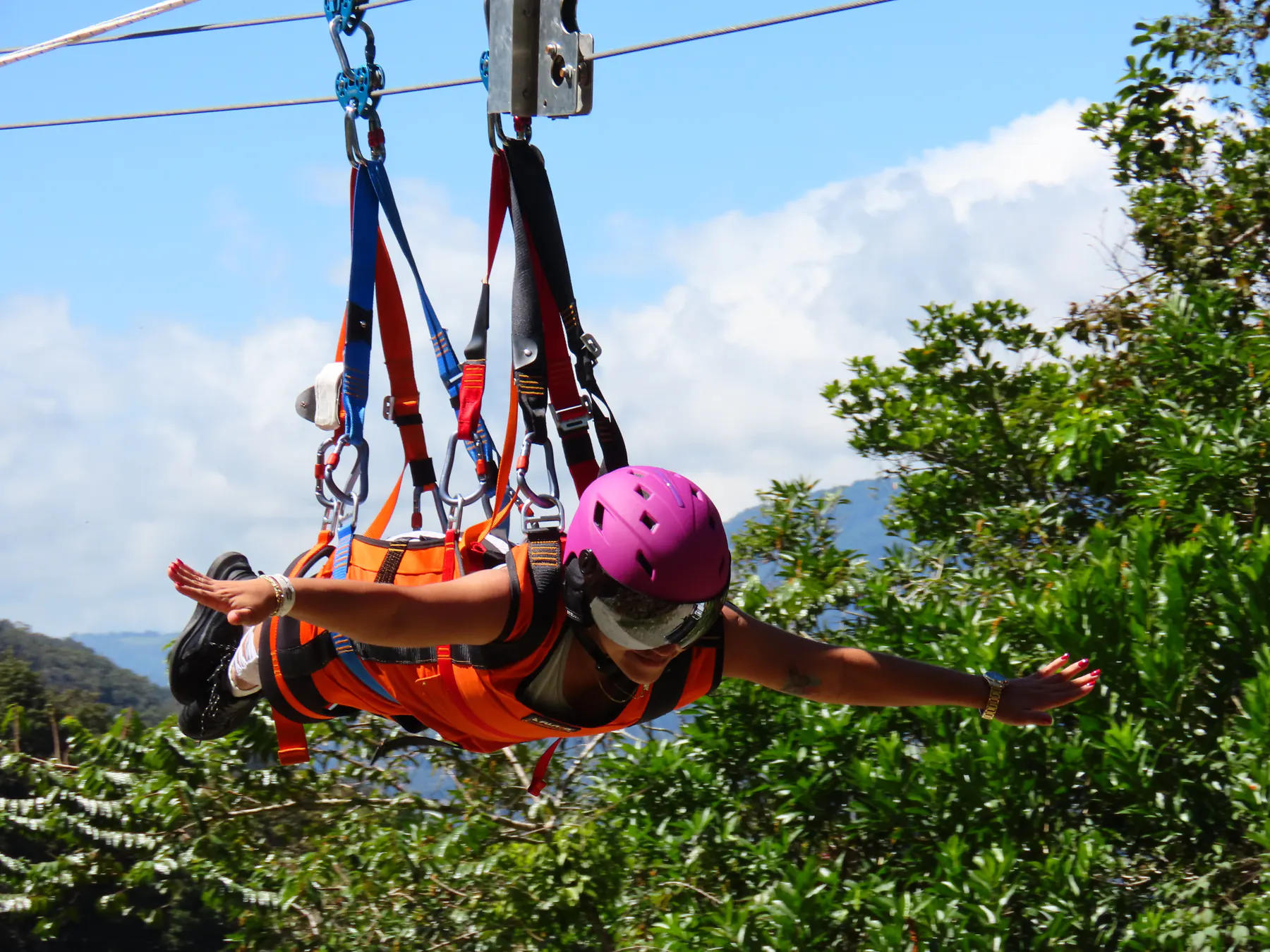 A rider flying face-first on the Superman zipline with blue sky and mountains behind