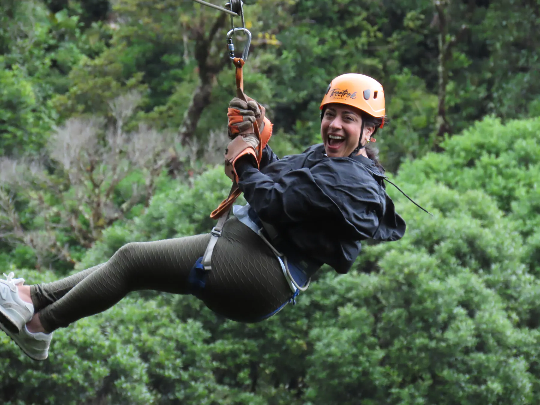 A woman laughing as she zips over the treetops on the canopy tour