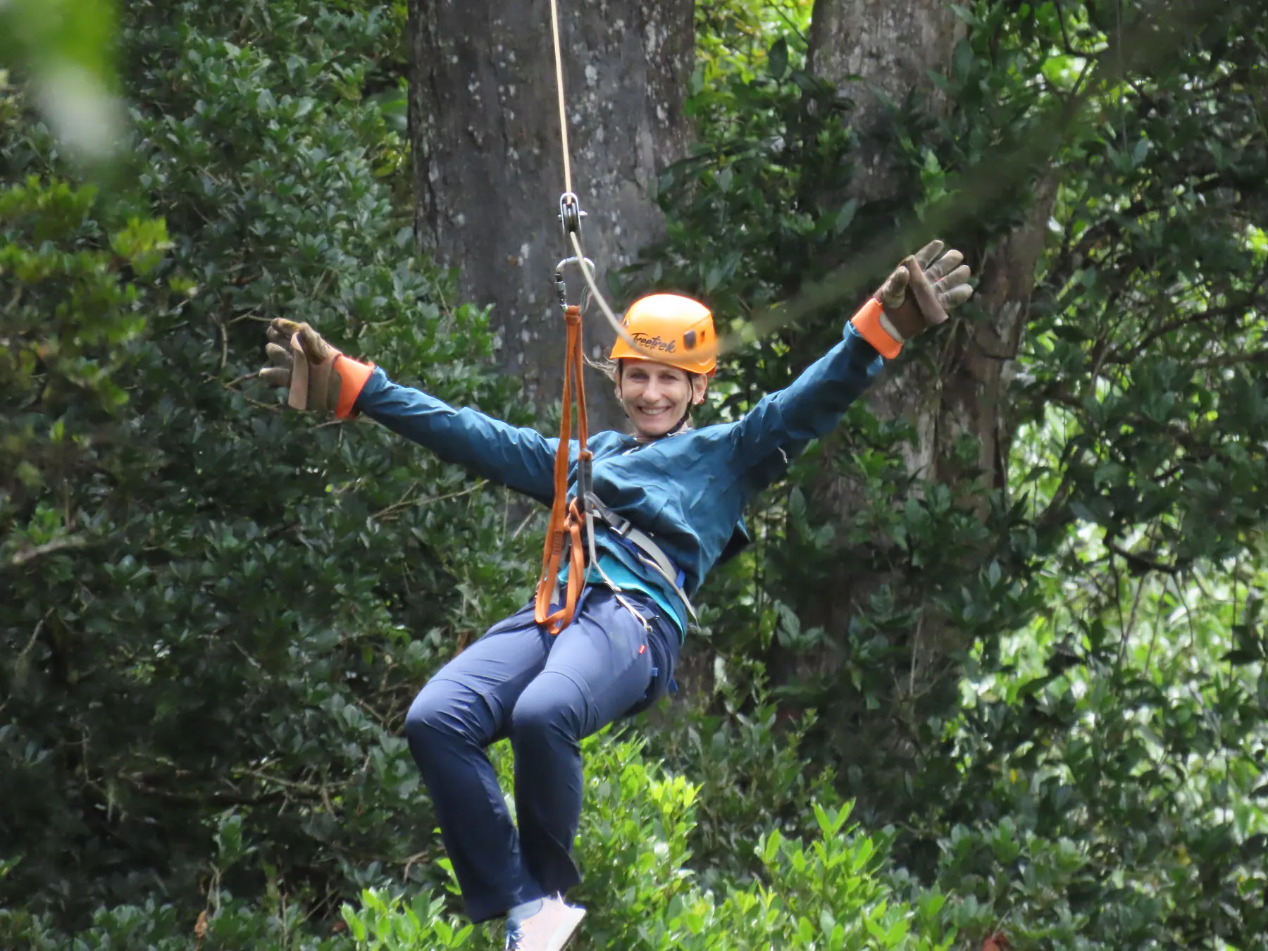 A smiling woman ziplining with her arms out through the Boquete treetops