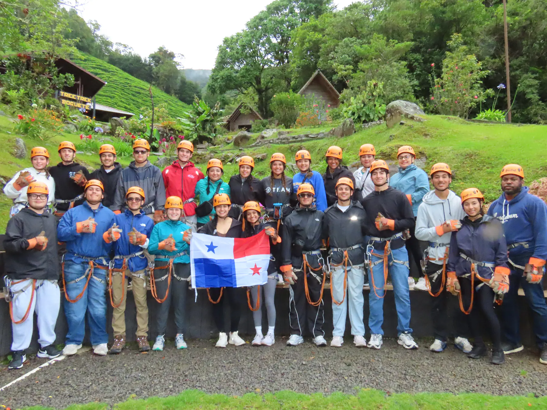 A large group in zipline gear holding a Panama flag before the canopy tour